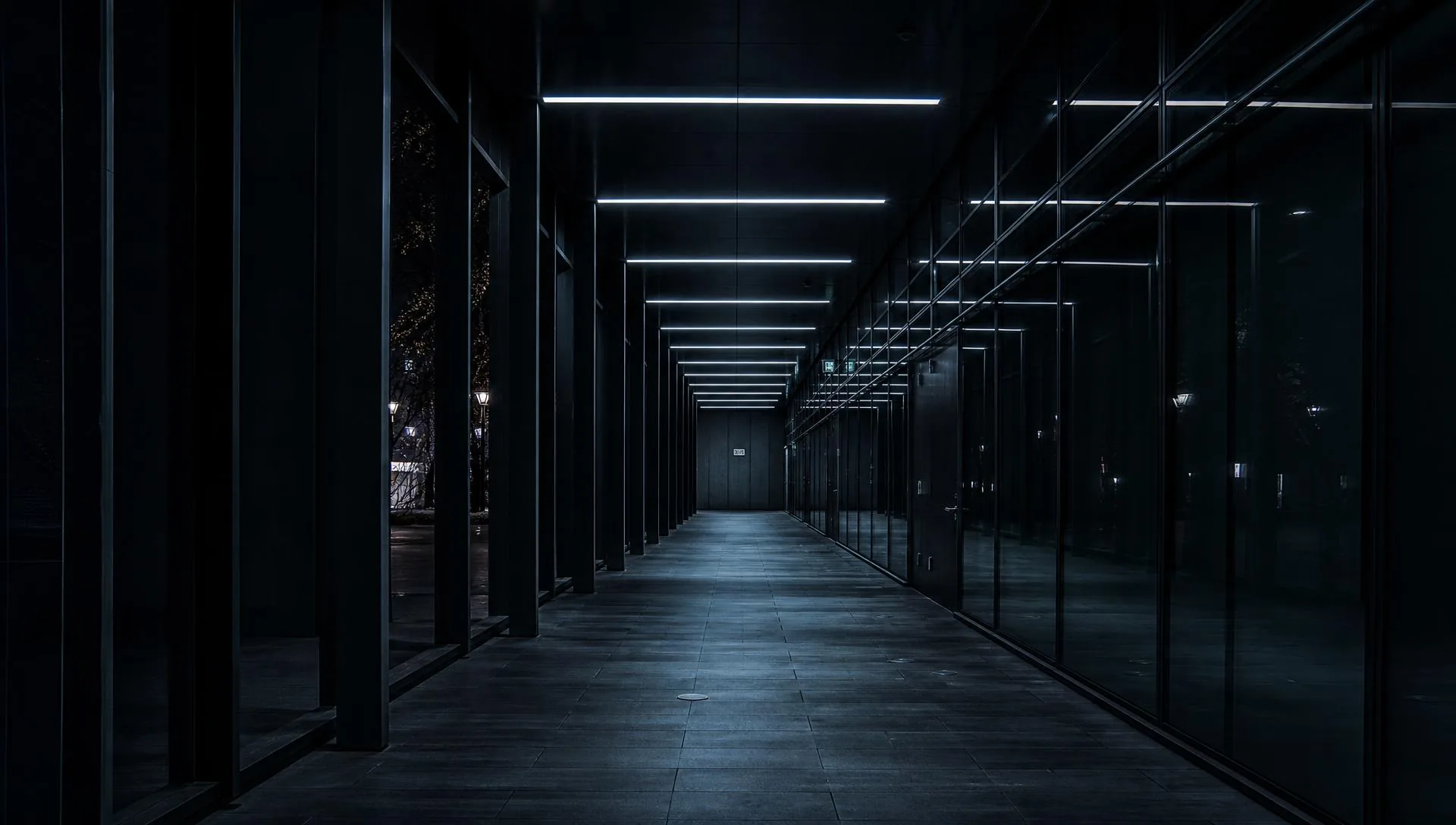 A dark glass and steel corridor at night with receding pale blue light lines