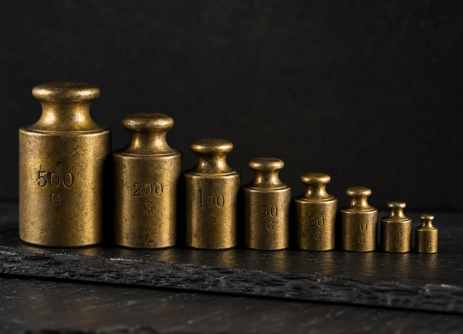 Graduated antique brass balance weights arranged on dark slate